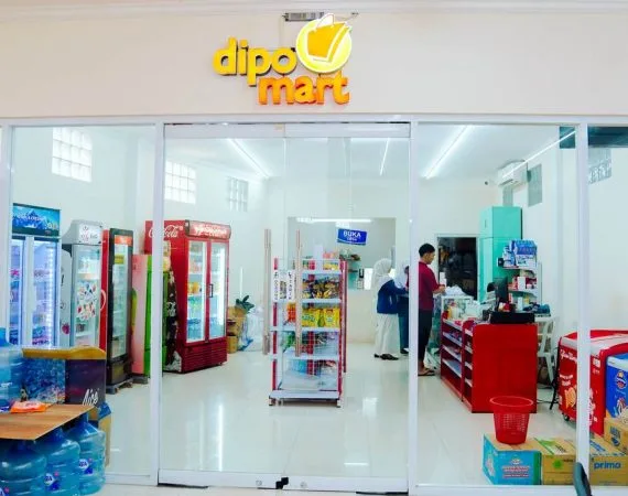 Koperasi sekolah berpapan nama Dipo Mart dengan pintu kaca, lemari pendingin minuman dan rak barang; dua orang berada di dalam