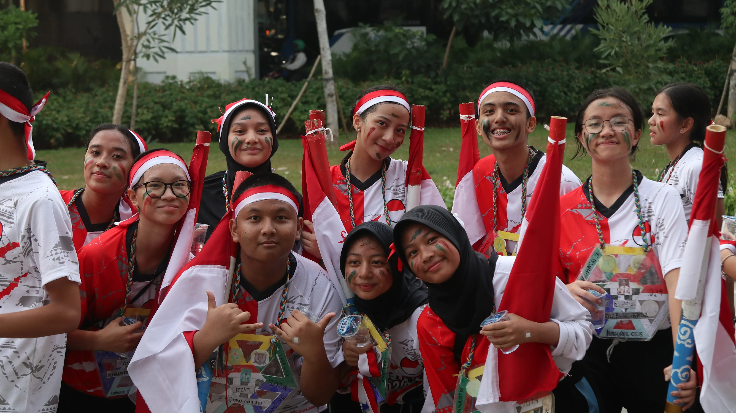 Siswa pengurus OSIS berkaus merah putih dengan coretan wajah dan properti bambu berbendera pada sebuah kegiatan di halaman berumput